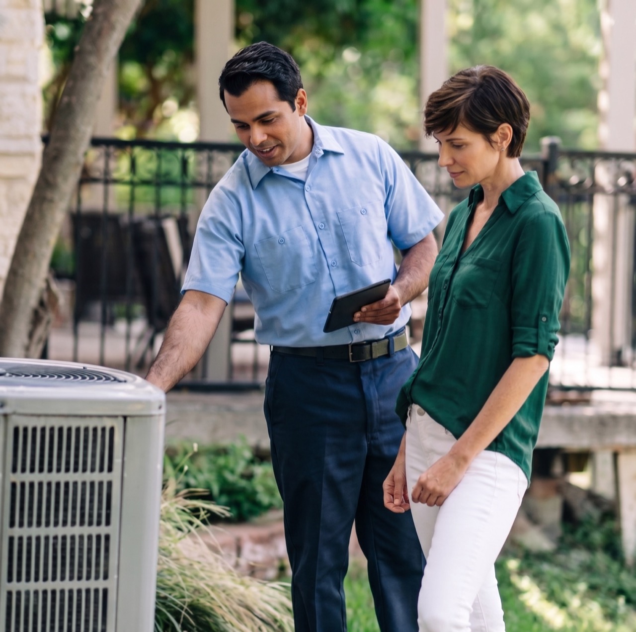HVAC technician with a tablet reviewing an outdoor AC unit with a homeowner