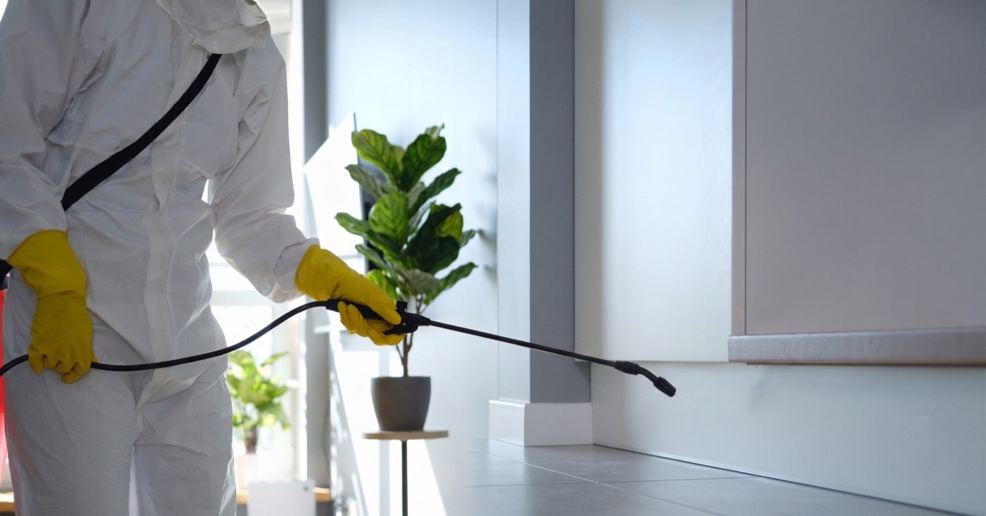 Pest control technician in a protective suit and gloves spraying treatment indoors